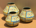 Set of three graduated hand-painted Rajasthani metal pots with faceted vertical ivory panels, pink and yellow floral sprigs, blue scrolling vine border and iron ring handles