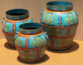 Set of three graduated hand-painted Rajasthani metal barrel pots with sky blue folk-art floral panel body, dark teal flared collar rim, gold panel borders and teal loop handles