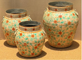 Set of three graduated hand-painted Rajasthani metal urns in chalky cream with loose botanical coral-orange flowers, teal-green leaf clusters and white loop handles