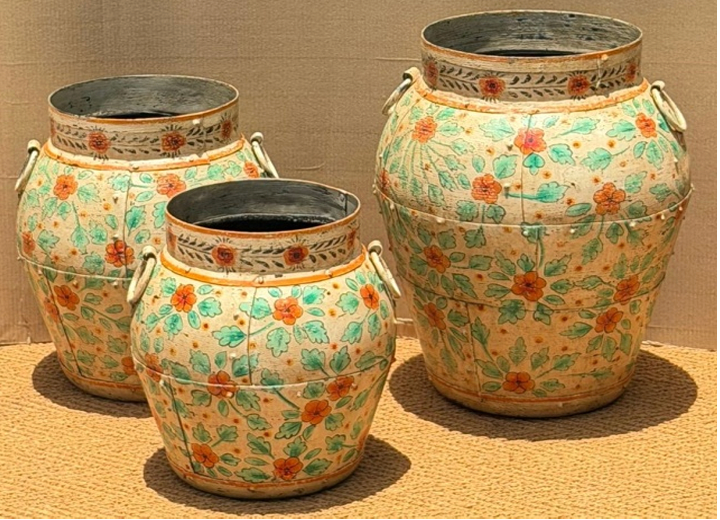 Set of three graduated hand-painted Rajasthani metal urns in chalky cream with loose botanical coral-orange flowers, teal-green leaf clusters and white loop handles