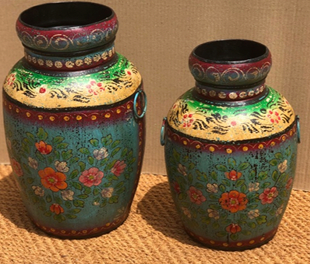 Two hand-painted metal urn vases in teal dark green with wide ivory yellow shoulder, dark scrolling vine, dot-work border, large scattered red pink coral floral scene and iron ring handles