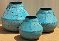 Set of three distressed iron wide-shoulder pots in heavily cracked and chipped sky blue turquoise finish with riveted panel seams radiating from neck, wide flat shoulder dropping to narrow base and iron ring handles on each side