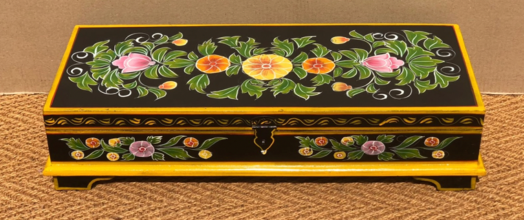Hand-painted mango wood keepsake box in jet black with gold border banding, central floral garland lid featuring yellow dahlia, pink roses and dark green leaves on black ground, iron clasp and four bracket feet